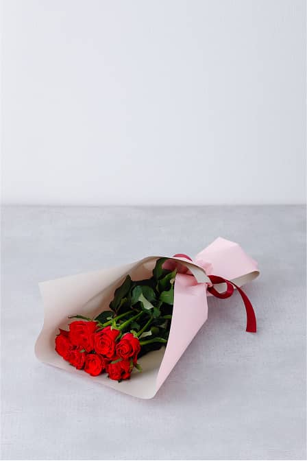 ピンクのラッピングに包まれた赤いバラの花束が横向きに置かれている。