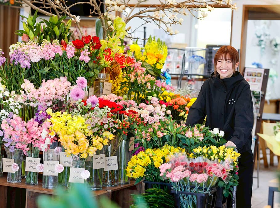 花屋の店内で色とりどりの花々に囲まれて笑顔を見せる女性スタッフ