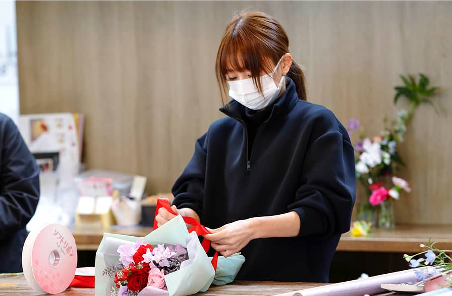 フラワーショップで花束に赤いリボンを結ぶ女性スタッフ、丁寧なラッピング作業中。