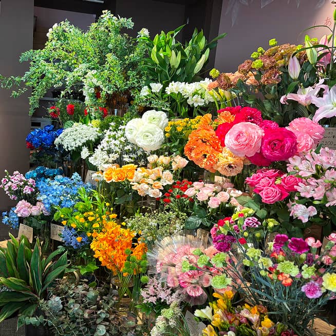 様々な種類の花が豊富に並べられた花屋の店内。色鮮やかなバラ、ユリ、ラナンキュラスなどが目を引く。
