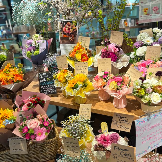 様々な色や形の花束やアレンジメントが展示された花屋の店内。特に「Flower Cakes」と書かれた札があり、花をケーキのように見立てた商品も並んでいる。