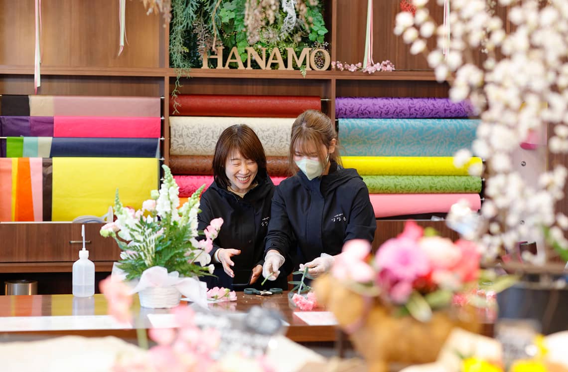 花屋で笑顔のスタッフ2人がフラワーアレンジメントを制作している様子